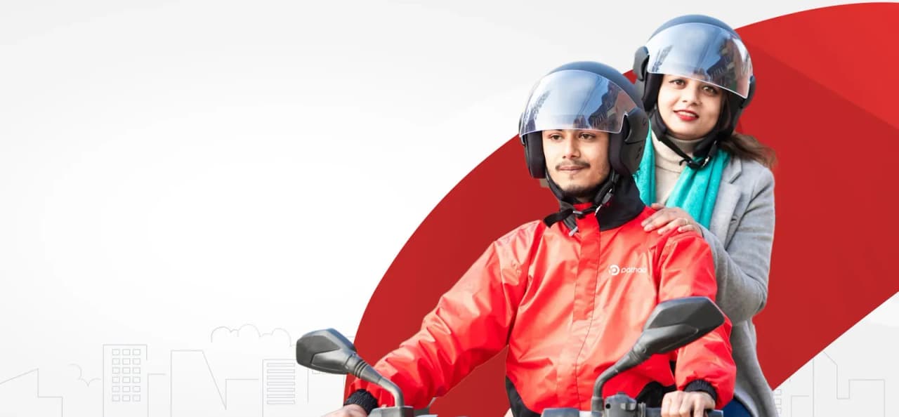 A man and a woman on a scooter, both wearing helmets, with the man in a red jacket featuring the Pathao logo.