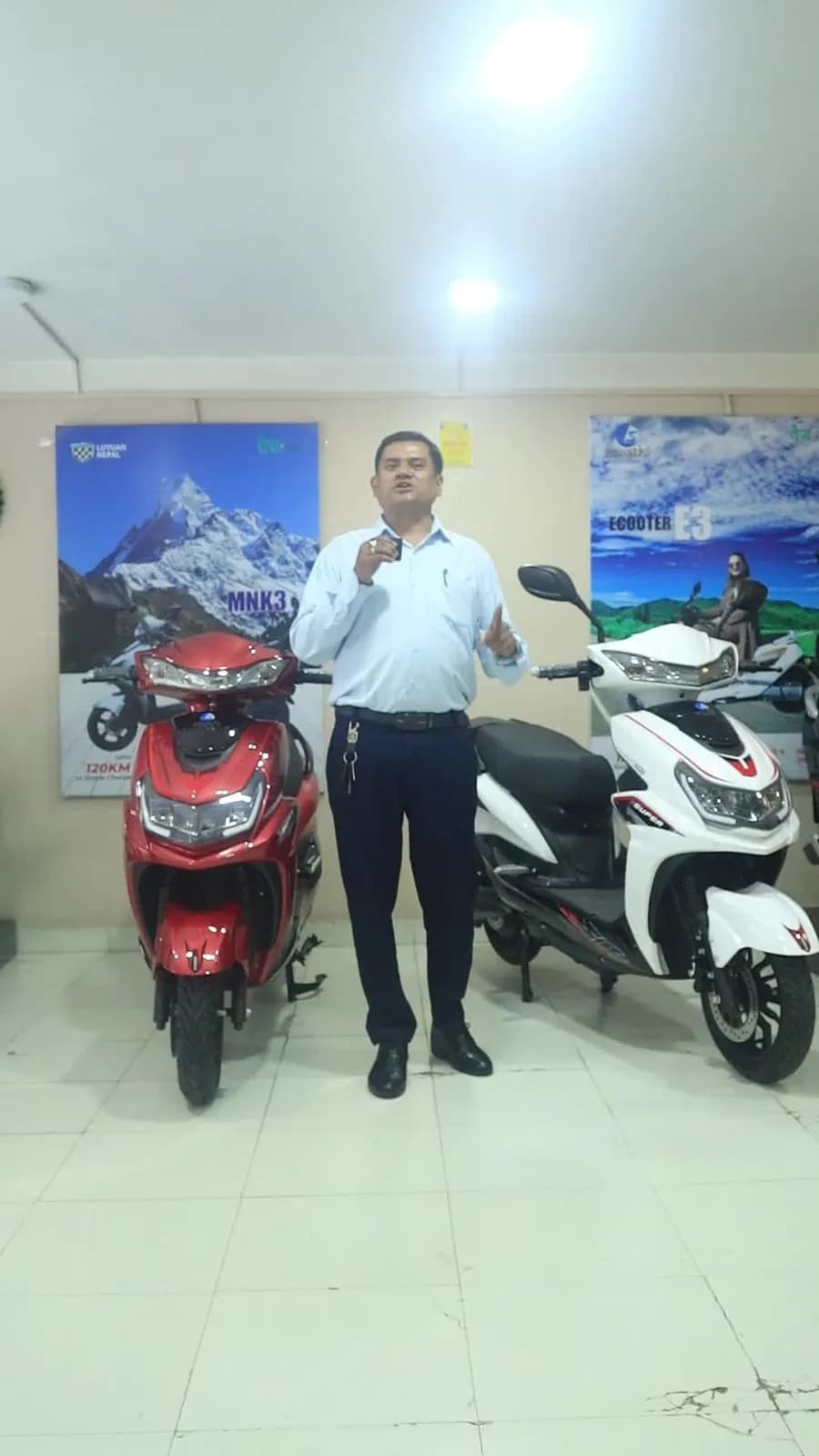 A man stands between a red and a white Sarathi E-Scooter in a showroom.