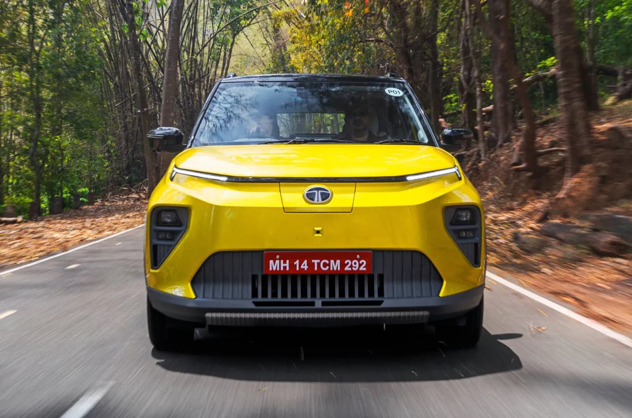 Front view of a yellow Tata Punch EV on a road surrounded by trees.